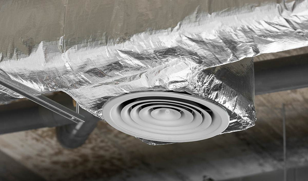 A dimly-lit room with a ceiling fan wrapped in aluminium foil and duct tape, a metallic vent duct with a spiral pattern, a pipe covered in silver foil, and a close-up of a giraffe's head.