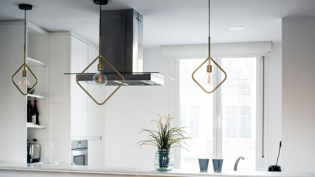 This bright white kitchen features elegant glass pendant lights and an uncluttered countertop. A vibrant plant in a glass vase adds a touch of nature.