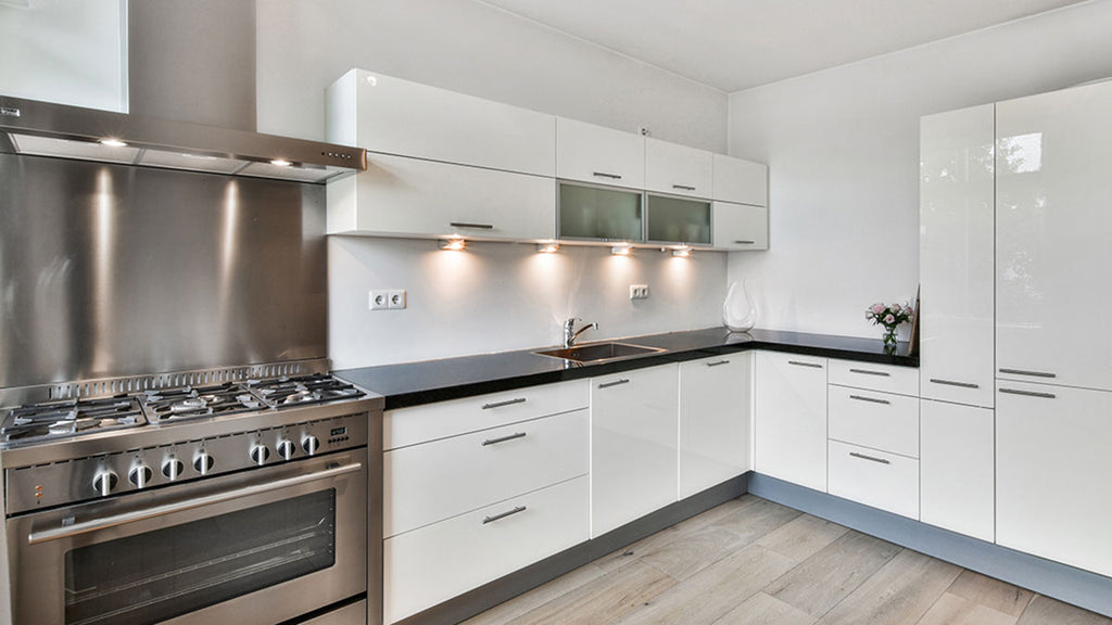 This modern kitchen features state-of-the-art stainless steel appliances, white cabinets, and black countertops. A vase of pink roses adds warmth.