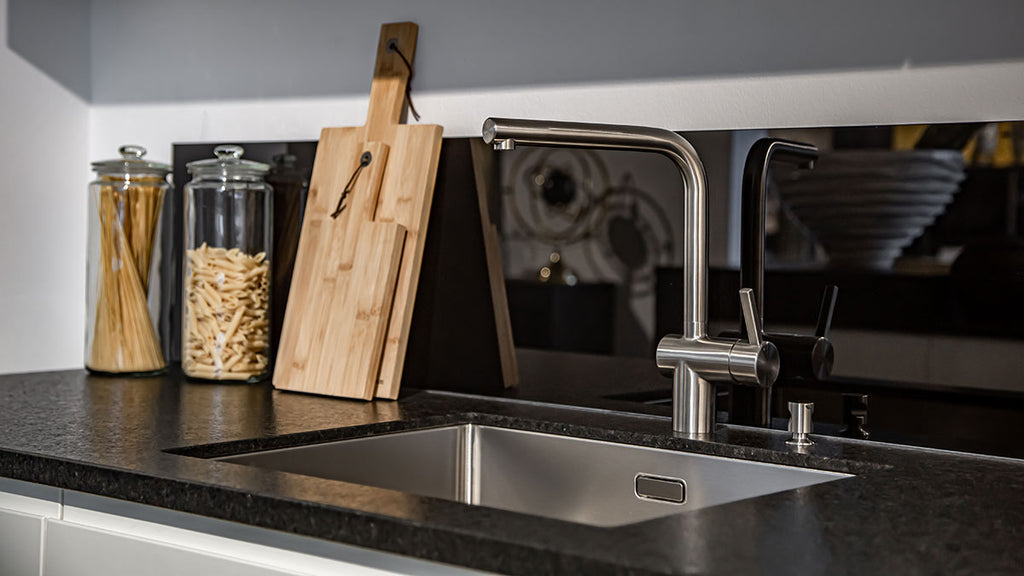 Sleek modern kitchen with stainless steel sink, black countertops, glass jar with pasta, wooden cutting board, and utensils.