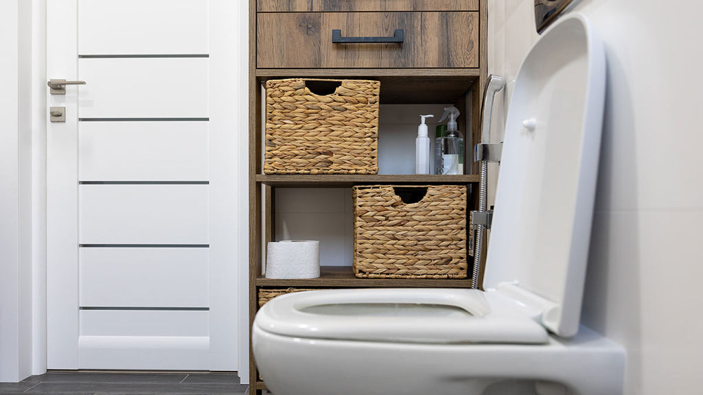 Modest bathroom with classic white toilet, wooden shelf, and neatly organised wicker baskets.