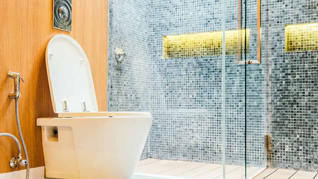Contemporary bathroom with white toilet, glass shower enclosure, white and yellow tiled walls, circular mirror, and glass building with yellow light.