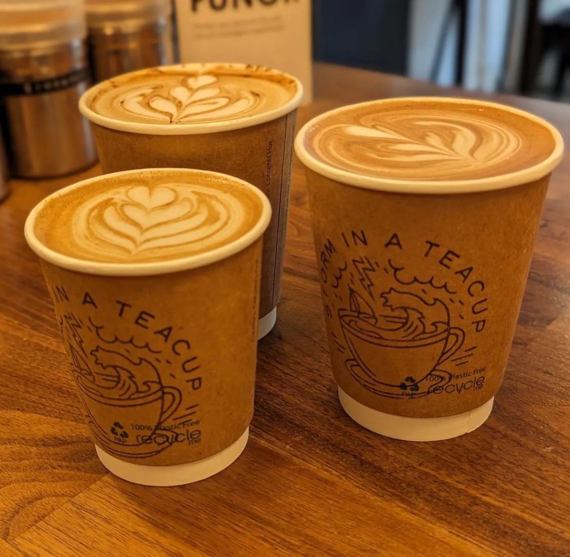 Three cups of coffee with latte art in recyclable paper cups on a wooden table.