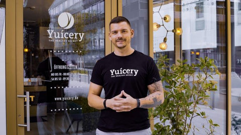 A male juice business owner in a black tee standing outside a store front.