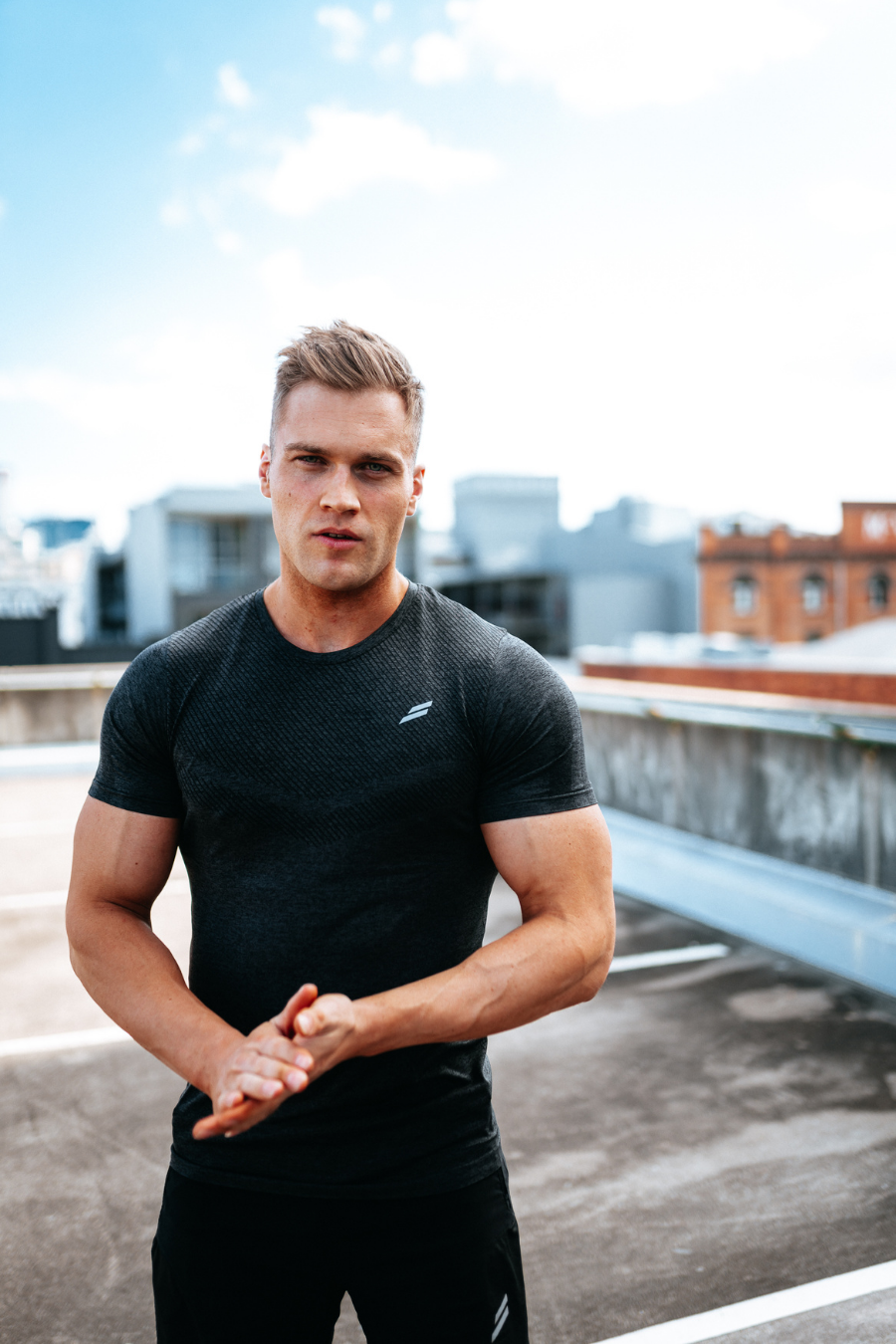 Male fitness models poses on a rooftop with hands clasped wearing Doyoueven focus seamless