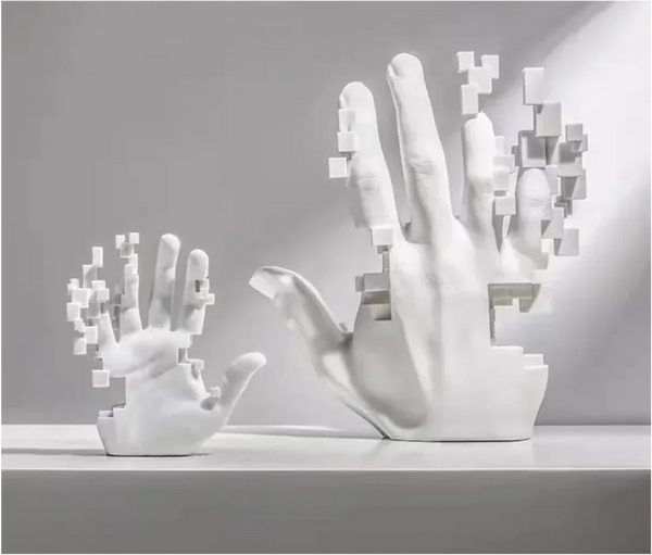 A **Handcrafted White Resin Art Statue for Home Decor - Modern Simplicity Design** by **The Stuff Box** displays two fragmented white hands—one larger and one smaller—with pixel-like sections missing. This modern and elegant design is handcrafted from resin and placed on a flat surface against a plain gray background.