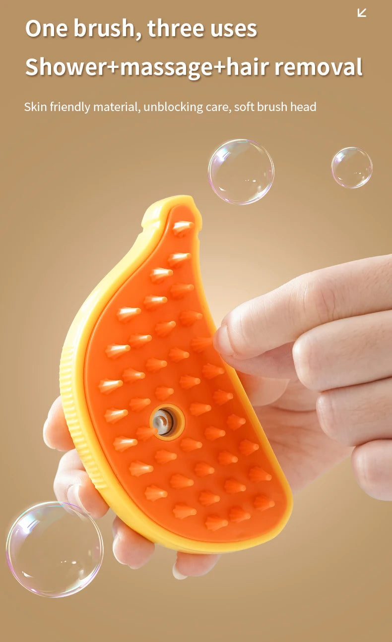 An orange handheld brush with a yellow grip is held near soap bubbles. The brush features pointed plastic bristles and is advertised as The Stuff Box 3-in-1 Electric Pet Grooming Brush - Cat Steam Brush for Massage, Hair Removal, and More! Text highlights its benefits.