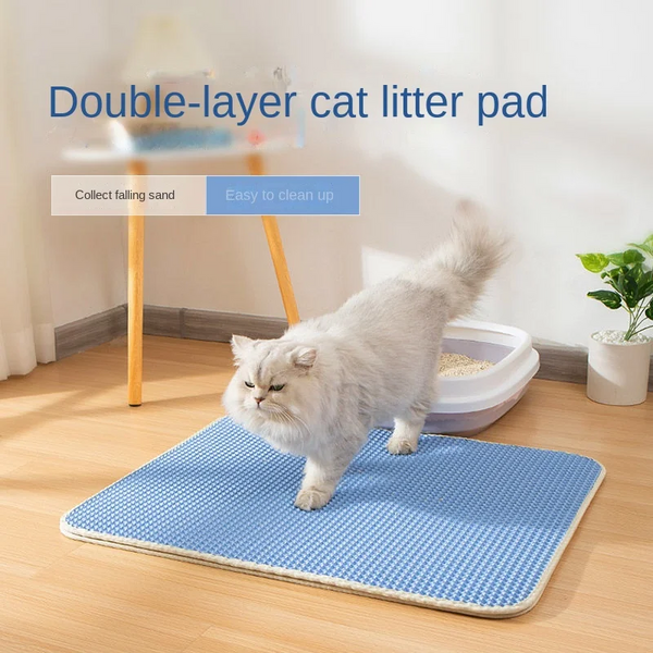 A fluffy cat walks on a blue **Waterproof Cat Litter Mat** by **The Stuff Box** placed on a wooden floor next to a litter box and a potted plant. Text on the image reads "Double-layer design" and "Easy to clean up".