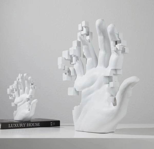 Two abstract white 3D-printed sculptures of hands with cubic segments removed, one placed near a book titled "Luxury House." The modern and elegant design evokes sophistication, like the Handcrafted White Resin Art Statue for Home Decor - Modern Simplicity Design by The Stuff Box.