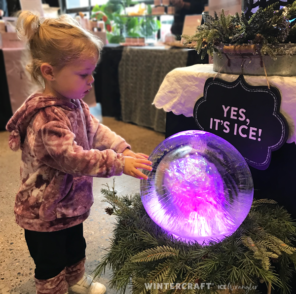 Young Wintercrafter enjoying the bright LED light in a large globe ice lantern at a holiday market. ice wrangler