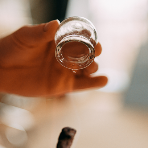 a round glass cup being held by a hand and a flaming cotton ball used to place heat in the cup.