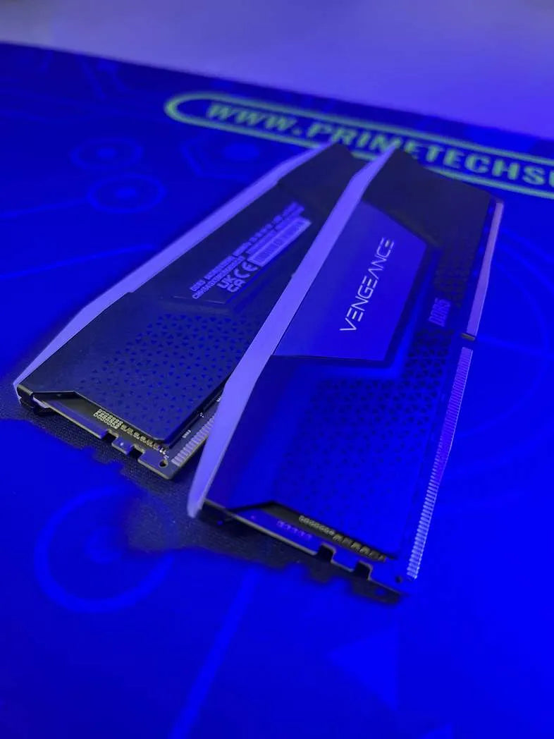 Dos módulos RAM iluminados en azul, etiquetados como 'V-GEN'. Se colocan sobre una superficie<!--nl--> con el texto 'www.prime-techs.com