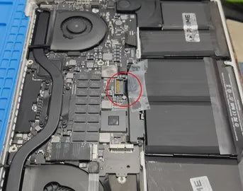 Vista interna de una computadora portátil que muestra componentes como el ventilador, la batería y los circuitos<!--nl--> sobre una alfombra de trabajo azul. El conector de la batería está resaltado con un círculo rojo<!--nl-->. Una etiqueta de la batería dice 'PRIME TECH SUPPORT', lo que sugiere<!--nl--> mantenimiento o piezas de Prime Tech Support en Miami, Florida.