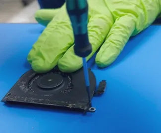 Close-up view of a technician from Prime Tech Support in Miami, Florida,
          using a screwdriver on a fan assembly, with green gloves visible against a
          blue background.