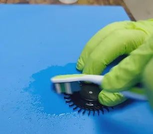 Un técnico de Prime Tech Support en Miami, Florida, con <!--nl--> guantes verdes, utiliza un cepillo para limpiar un componente del ventilador sobre una superficie azul húmeda