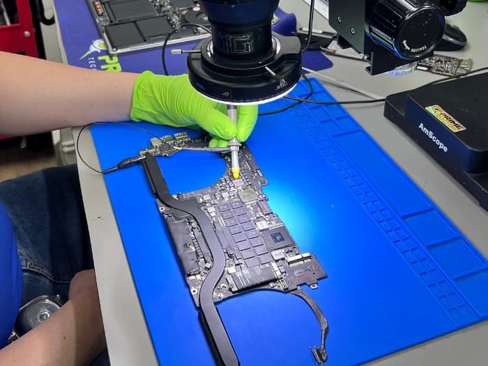 Prime Tech Support technician repairing a logic board of a Macbook Pro.