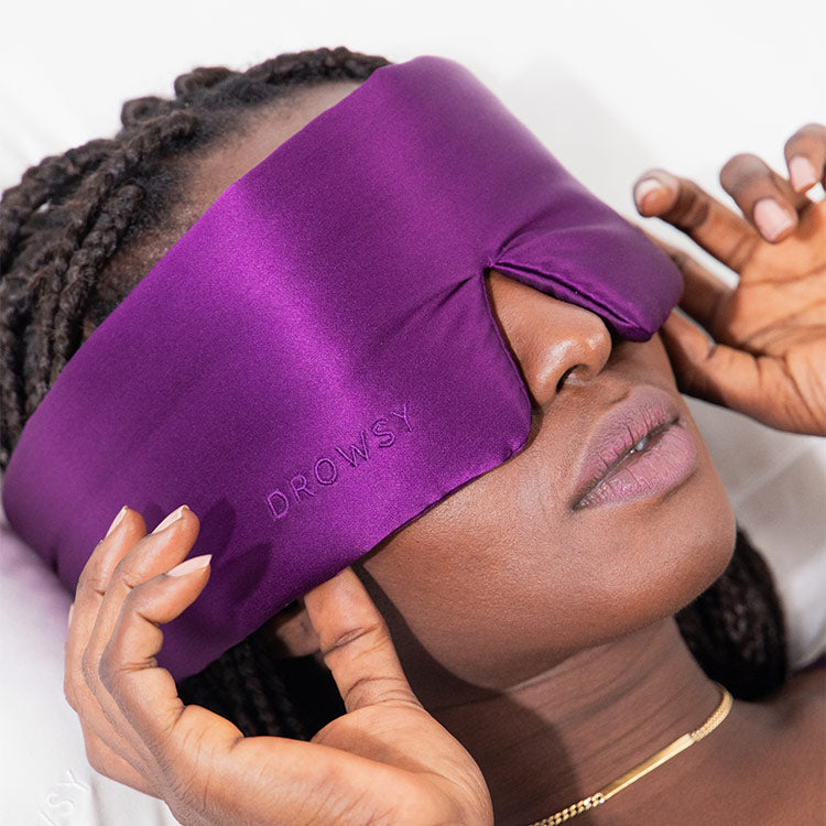 Model sleeping on white silk with a Drowsy black silk sleep mask covering her eyes