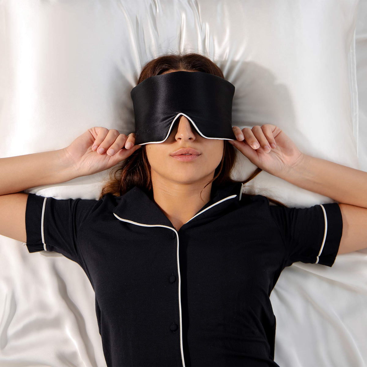 Model with black coloured Drowsy sleep mask covering eyes on white silk sheets