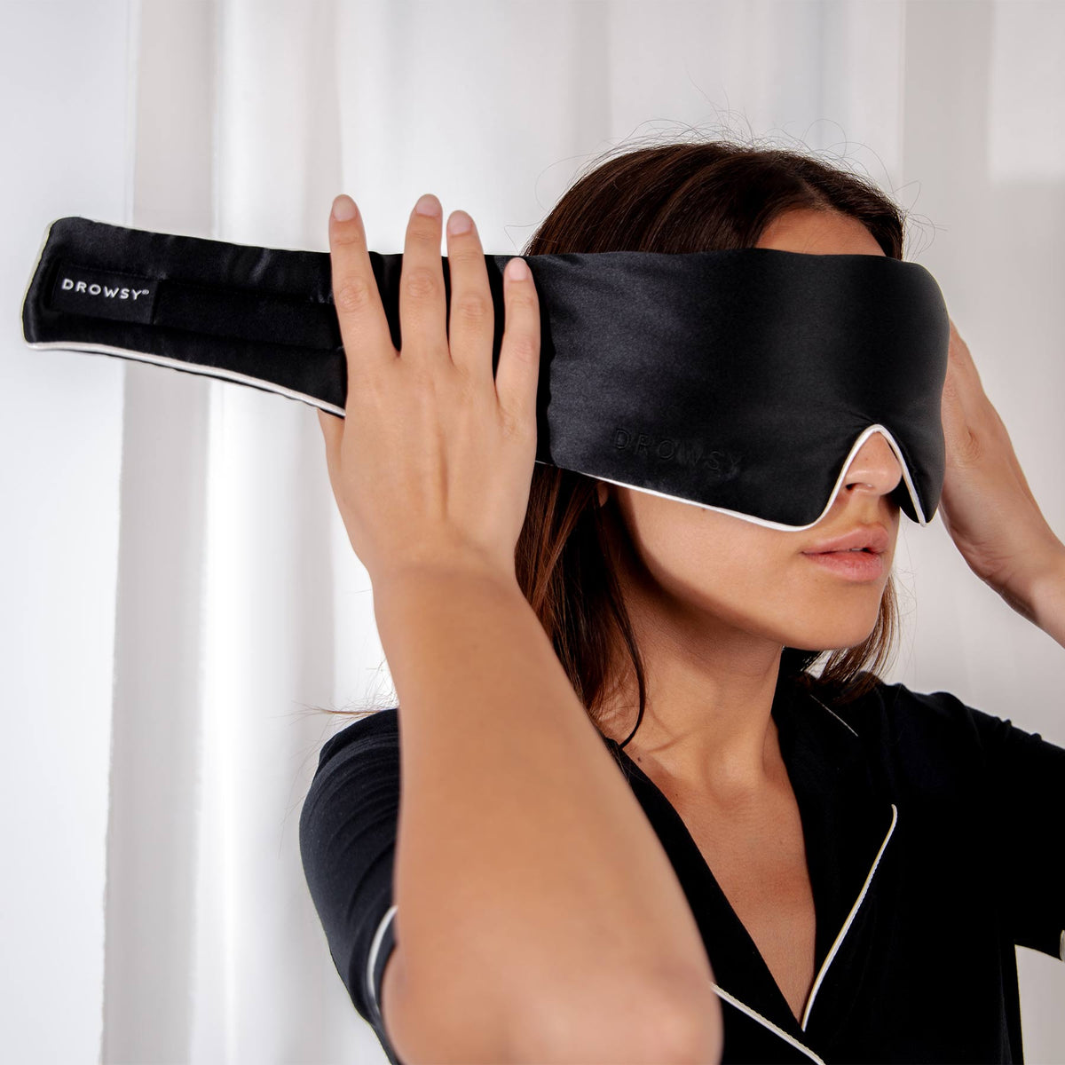 Model with black Drowsy sleep mask covering eyes with a white silk backdrop