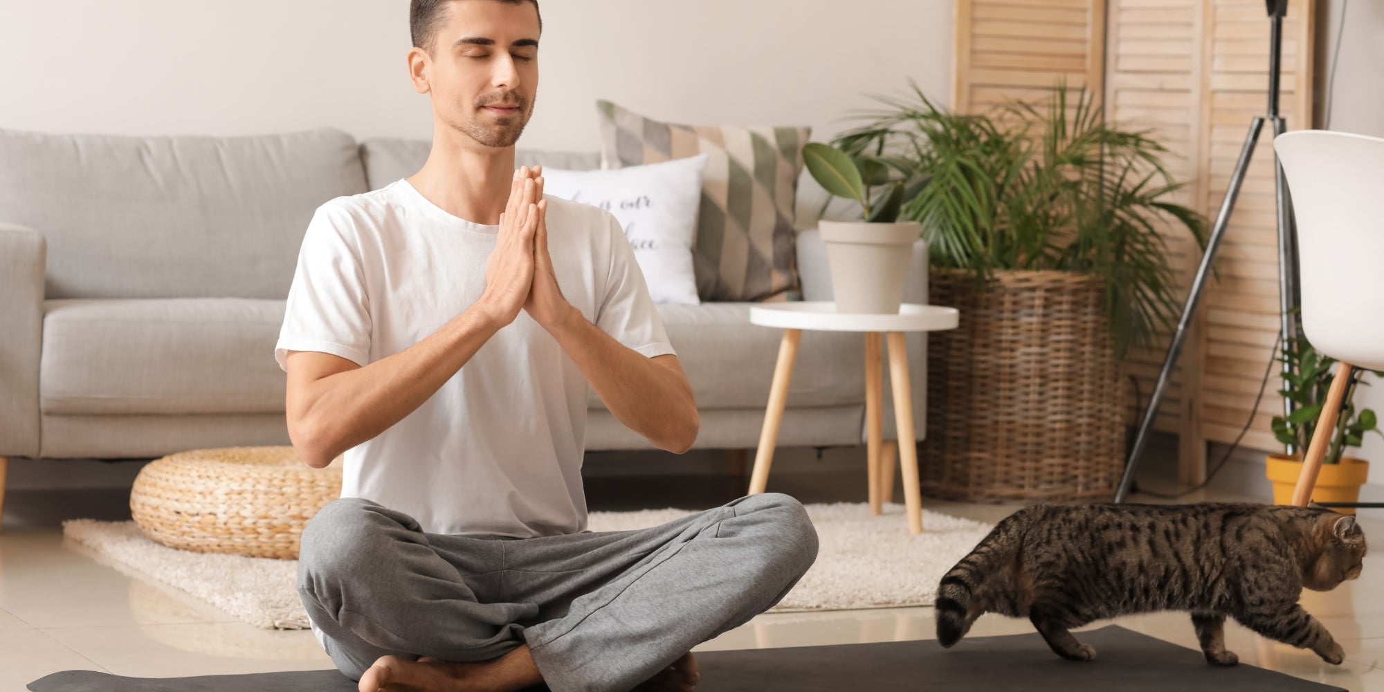 Joven con lindo gato meditando en casa