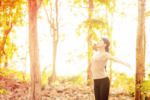 秋の森の中、運動や深呼吸をして肌の調子を整える女性