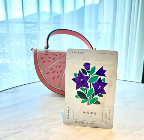 大峰堂の漢方錠剤　Hadaral十味敗毒湯　のパッケージ画像　アルミパウチ　紫の桔梗の花　西瓜柄のカバンと並んでいる