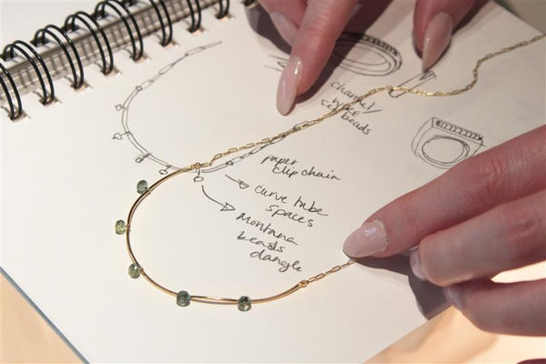 gold necklace with gold tubes and montana sapphire faceted beads laying on the sketch pad with the original design