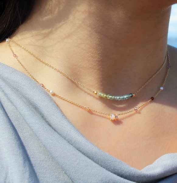young lady wearing  layering gold necklaces with teal, blue and green Montana sapphire faceted beads.