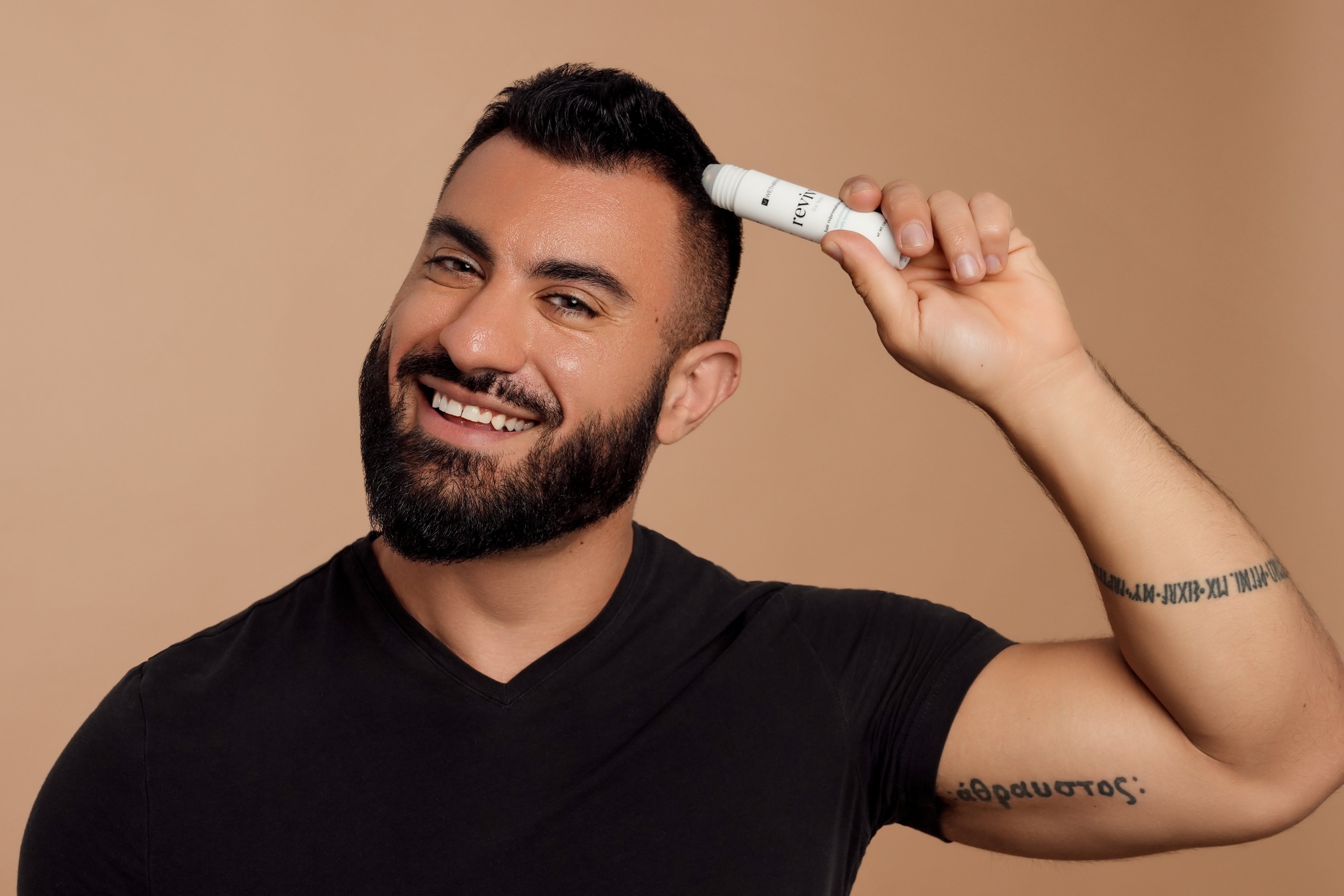 A man smiling and applying a hair product with a roller applicator.