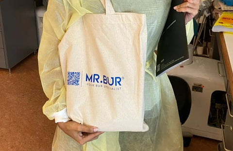 Dental student holding a Mr Bur tote bag that has the Logo on mr bur and inside has information about the dental burs that mr Bur sells worldwide