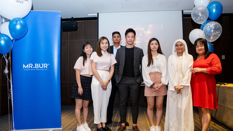 The employees at "Mr Bur" are taking a commemorative picture with the CEO Sean Yao next to them you can see a roll up stand that has the logo of mr bur the best dental bur supplier in the world