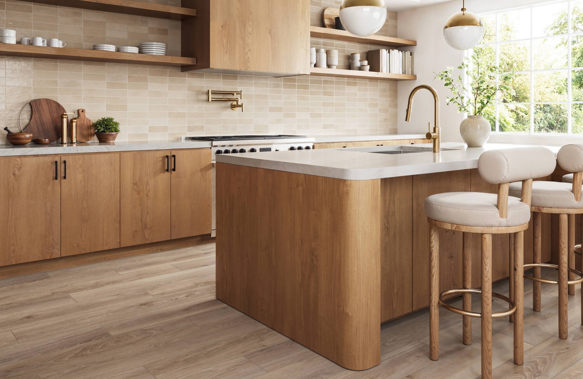 Modern kitchen with light wood cabinets, a white countertop island, beige tile backsplash, gold fixtures, and a beige wood look flooring.