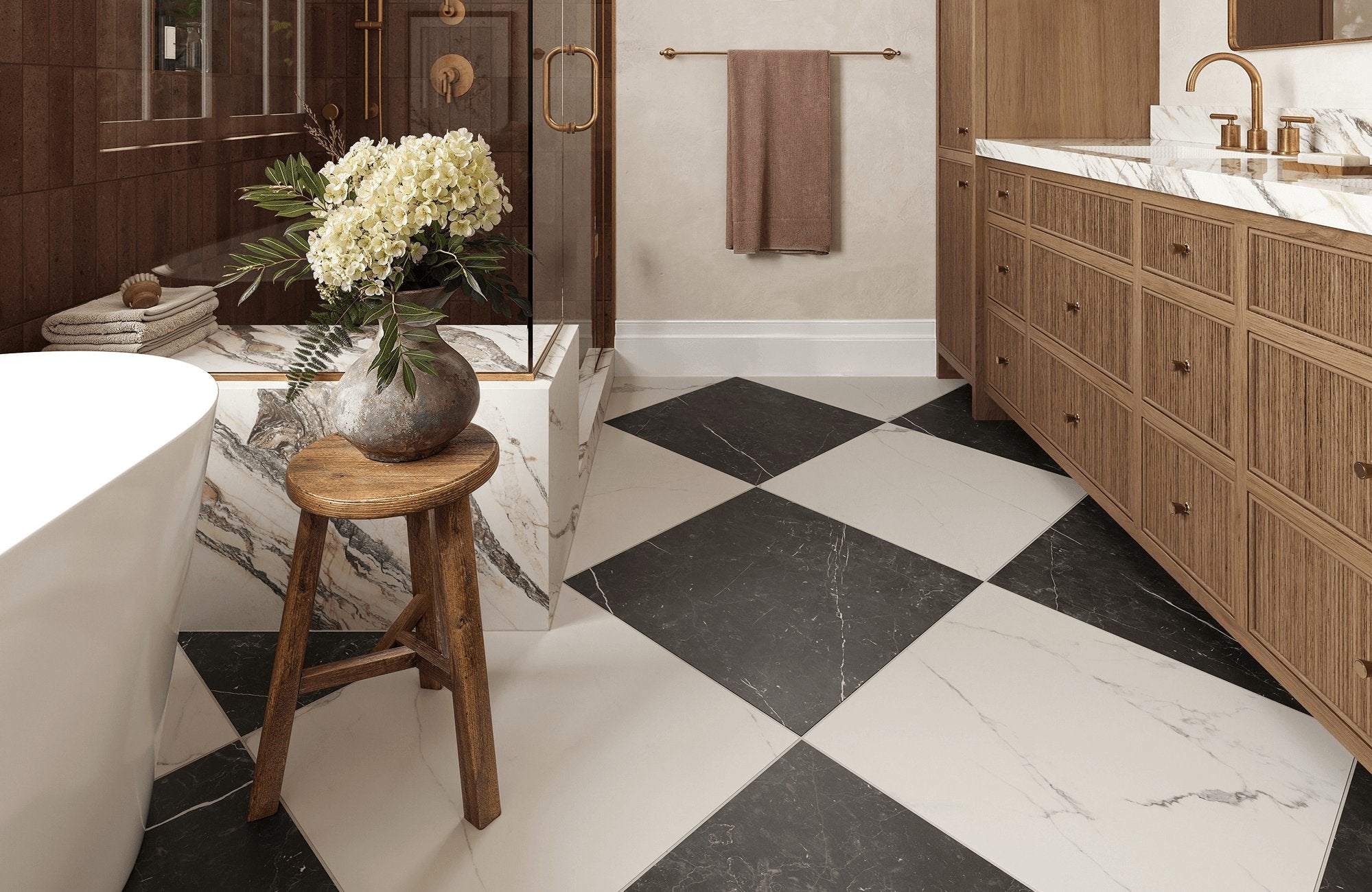 Sophisticated bathroom with black and white marble look checkered tile, wood cabinetry, gold fixtures, and a floral arrangement on a rustic stool.