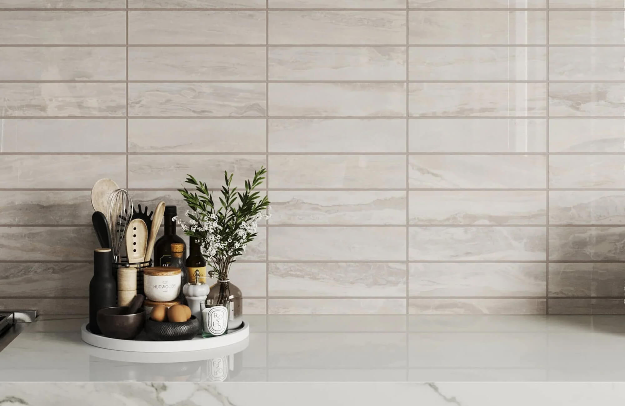 Modern kitchen with beige subway tiles, a marble countertop, and a stylish round tray holding utensils, oils, and a small plant