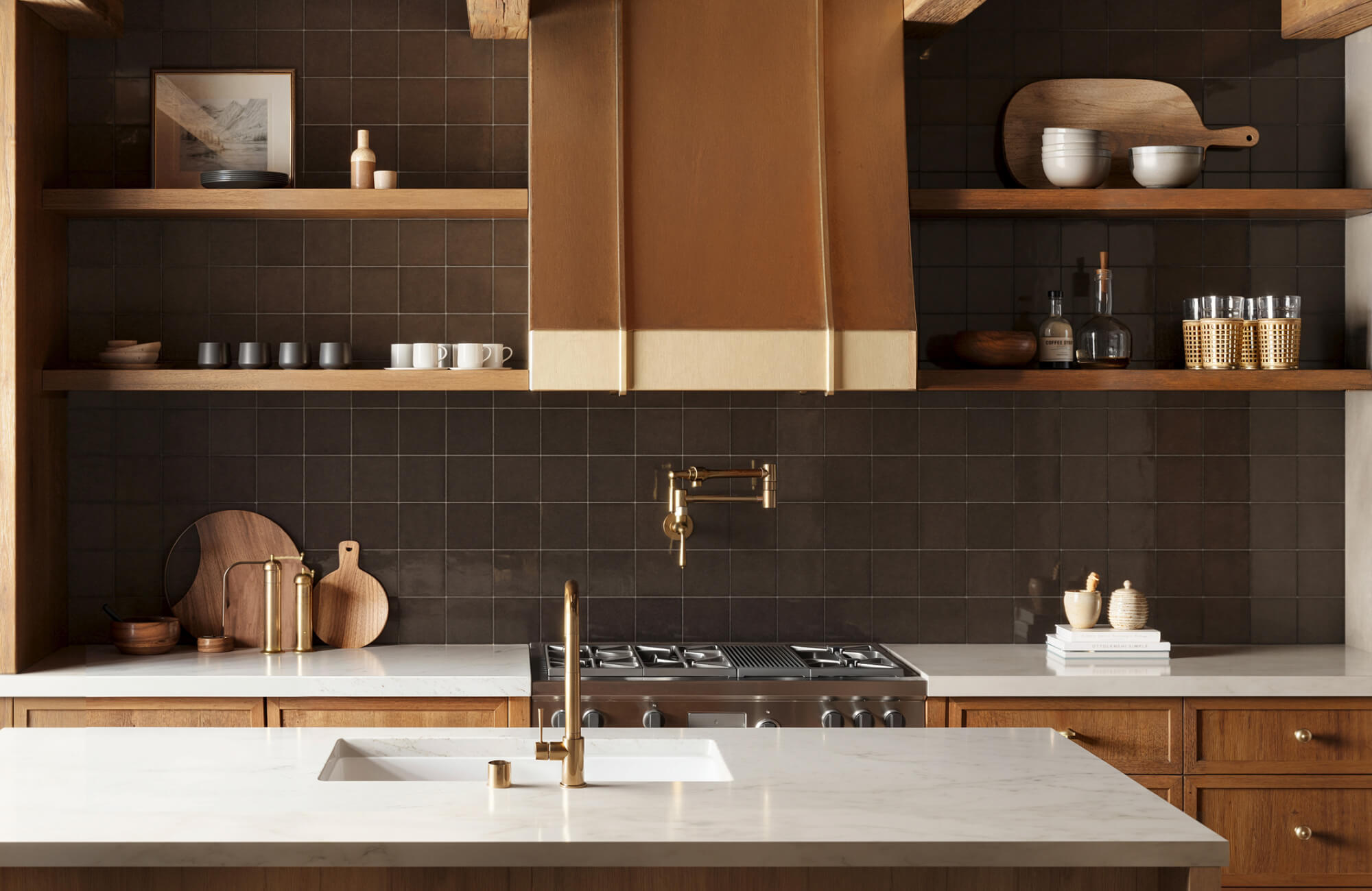 Modern rustic kitchen showcasing rich brown ceramic backsplash tiles, white countertops, open shelving, and a statement copper hood over a stainless steel stove.