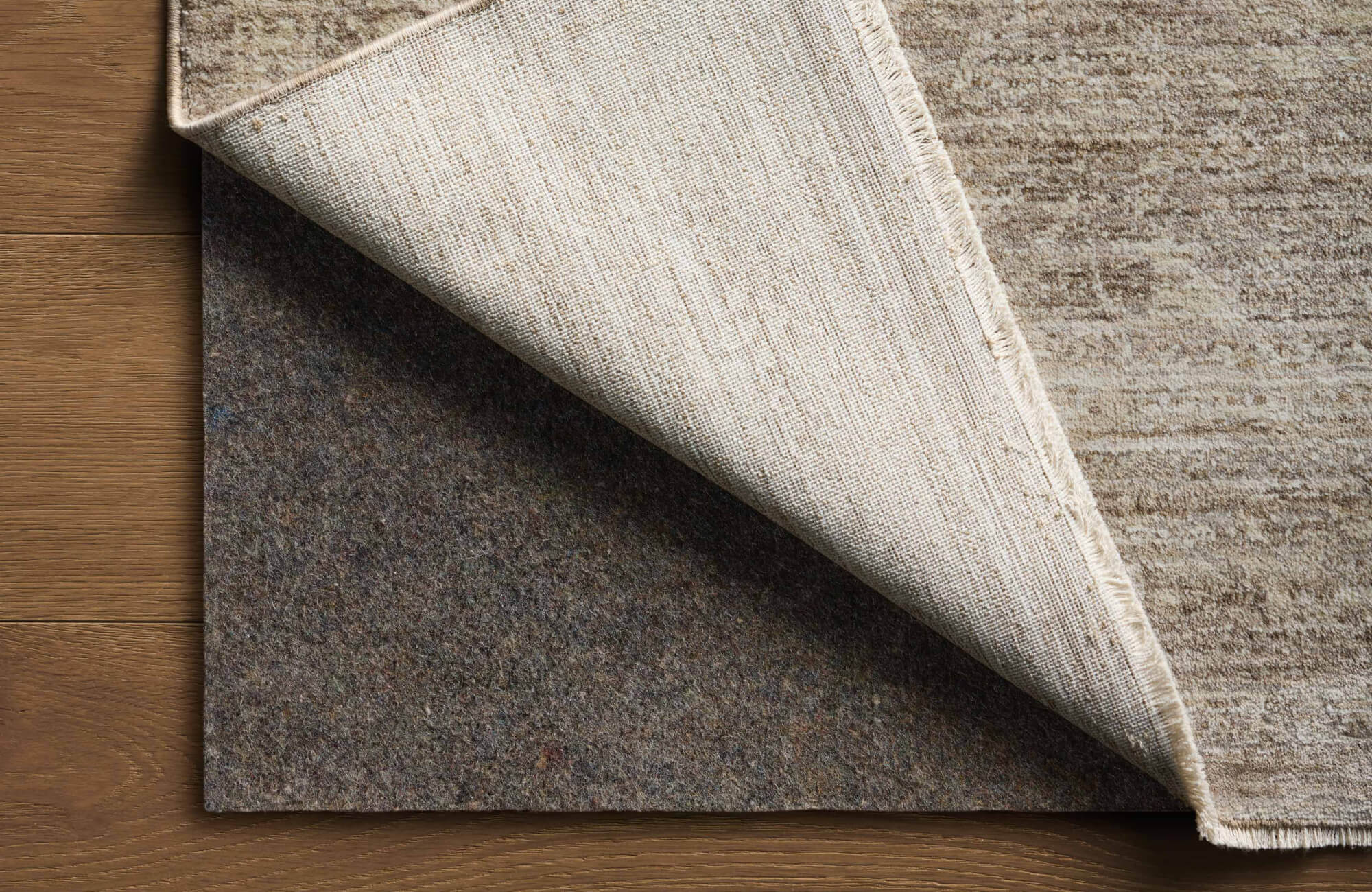 Close-up of the Haverford Polyester Pile Rug in Bronze / Oat, partially lifted to reveal its durable backing and plush texture.