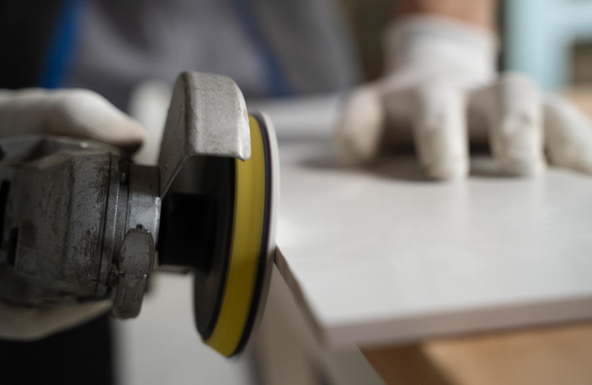 Close-up of a worker polishing the edge of a checkered tile with a grinding tool, wearing protective gloves for precision.