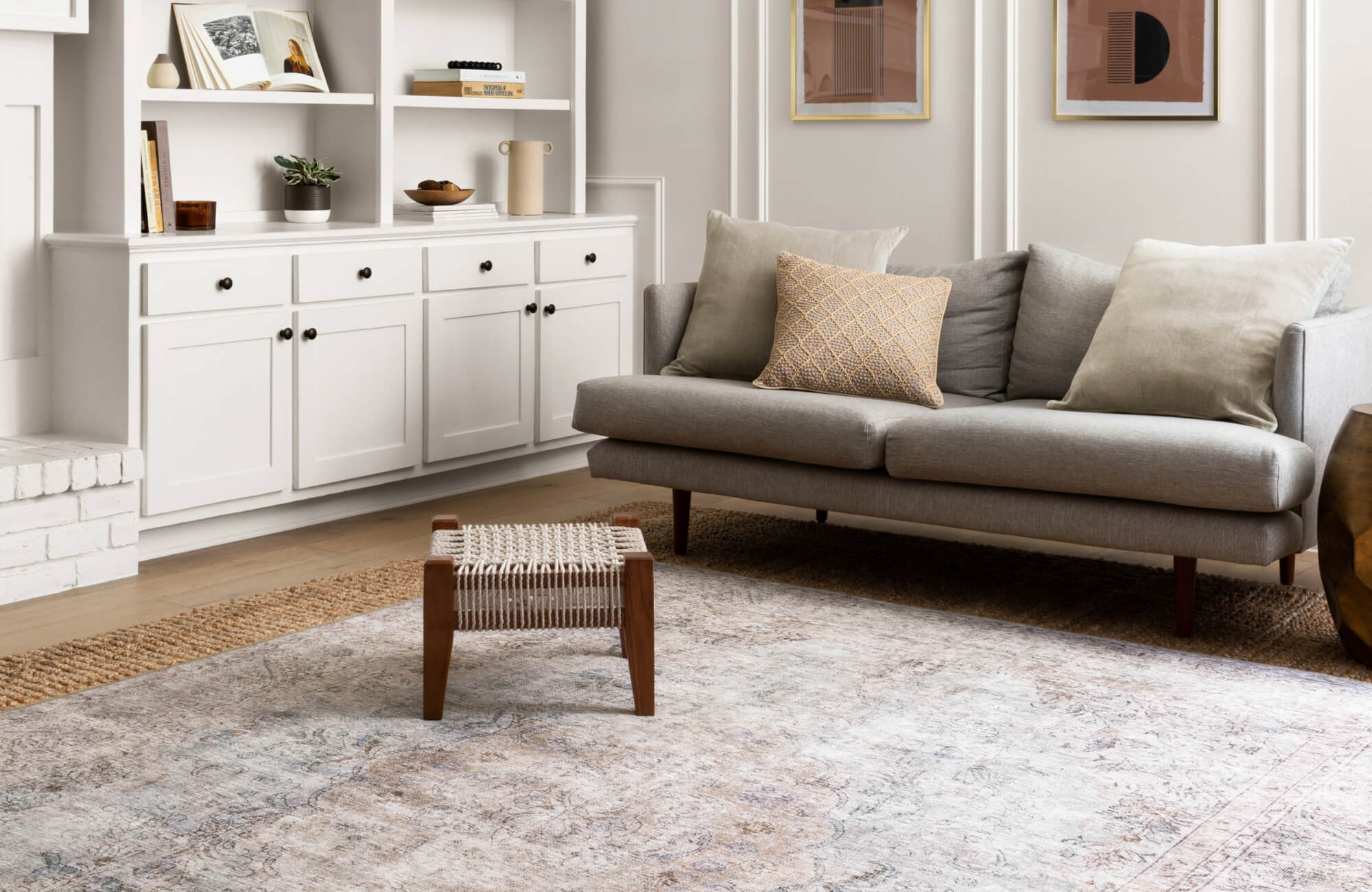 Neutral-toned living room with a spacious, faded large rug beneath a gray sofa and woven accent stool