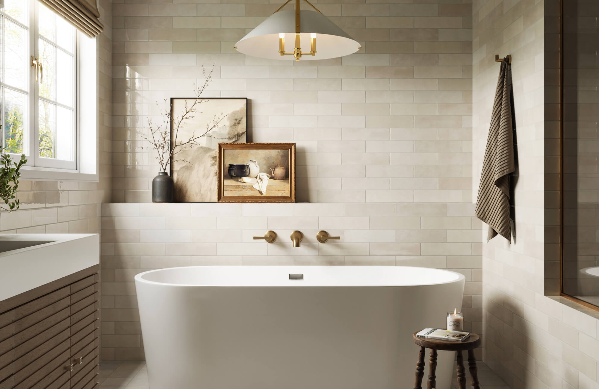 Soft beige ceramic subway tiles frame a freestanding tub with brass fixtures, styled with artful decor and warm natural light.