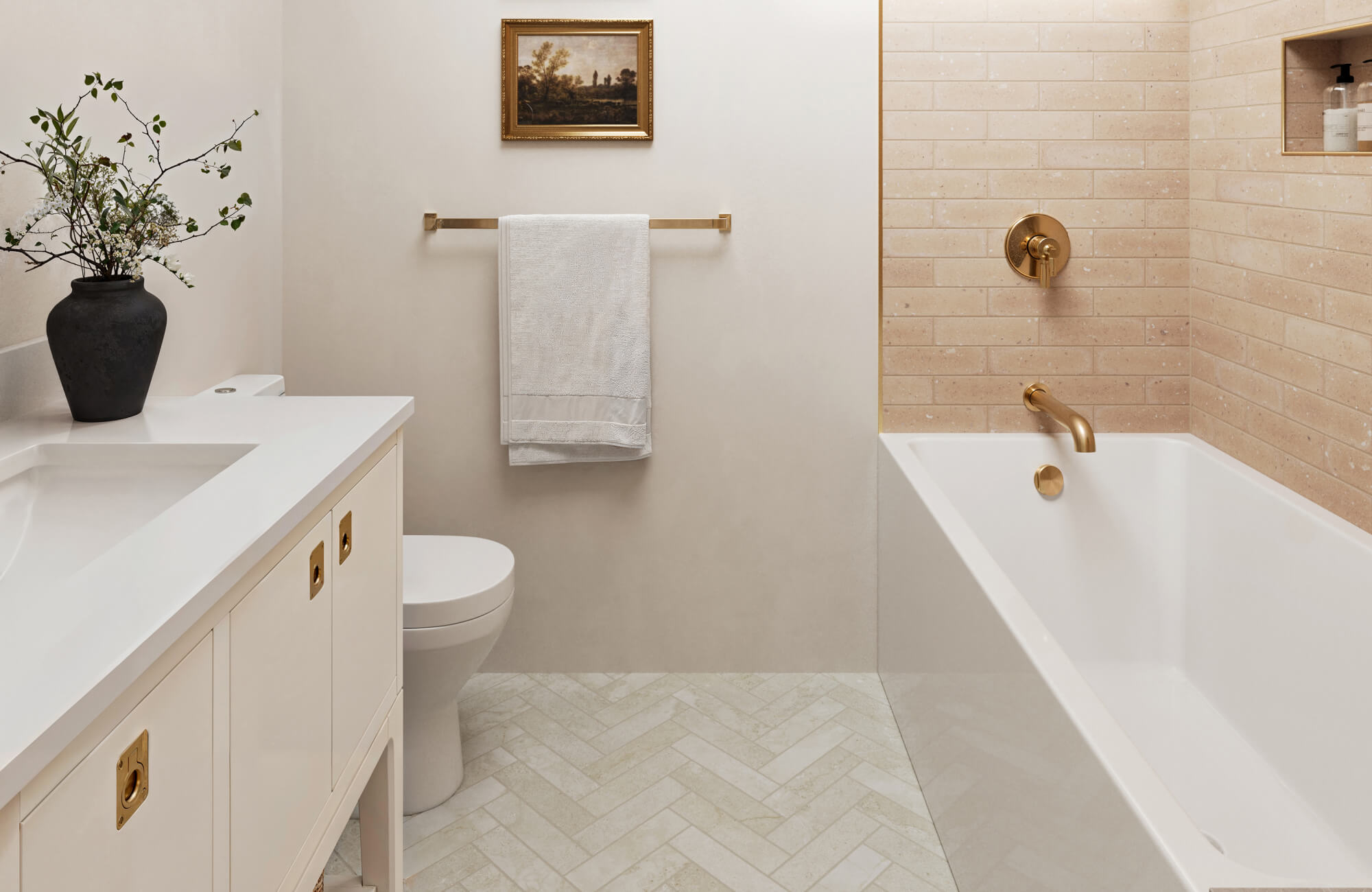Soft beige subway tiles and a herringbone floor make this bathroom feel more spacious, complemented by brass fixtures and a classic vanity.