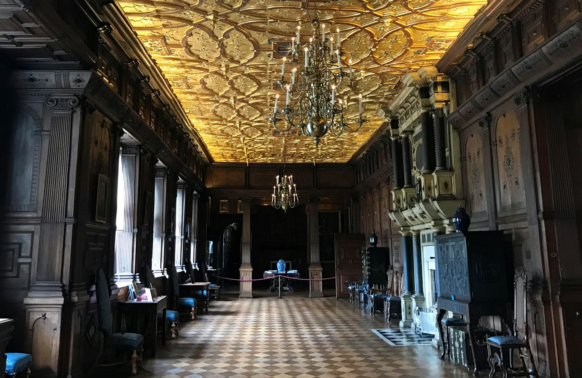 Luxurious hall with a golden coffered ceiling, intricate chandeliers, and checkered flooring, showcasing a blend of opulence and historical charm, an illustration of the dark academia interior style