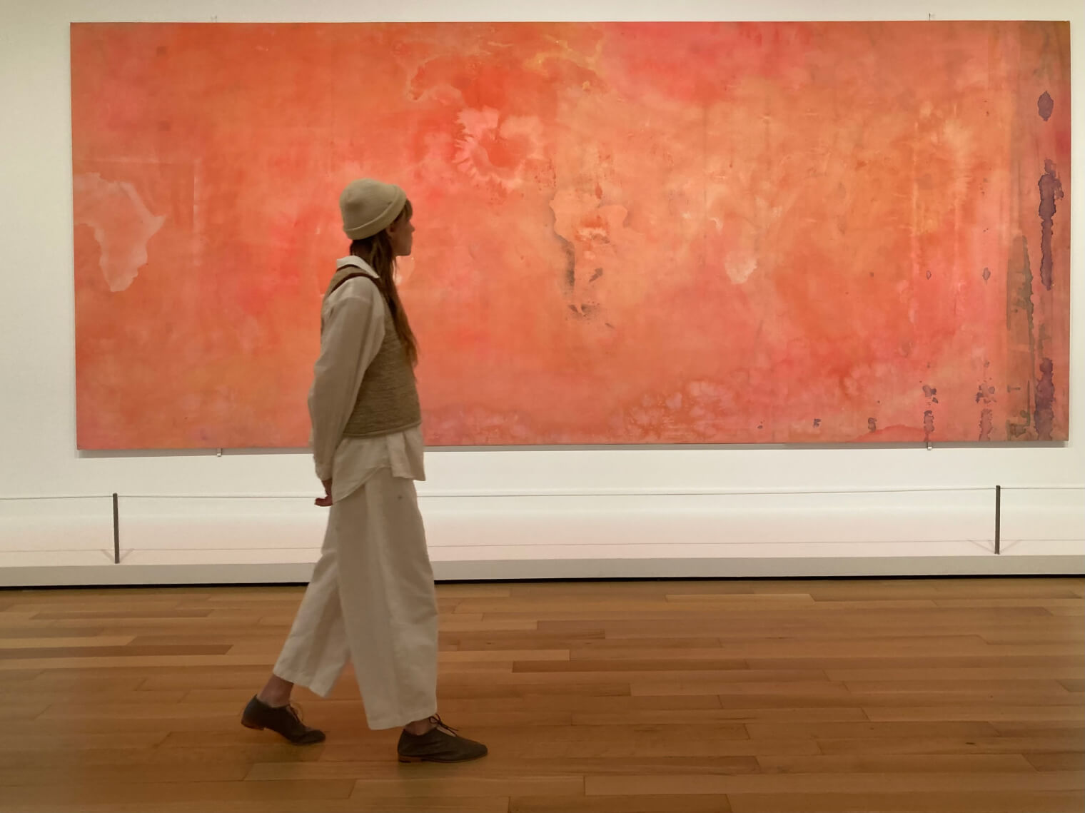 kate in white pants walking in front of a red painting 