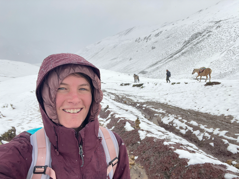 Ashley hiking up Rainbow Mountain with snow covering the ground and people guiding horses in the background