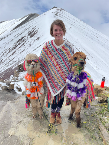 Ashley with two alpacas dressed in colorful attire at the top of Rainbow Mountain in Peru
