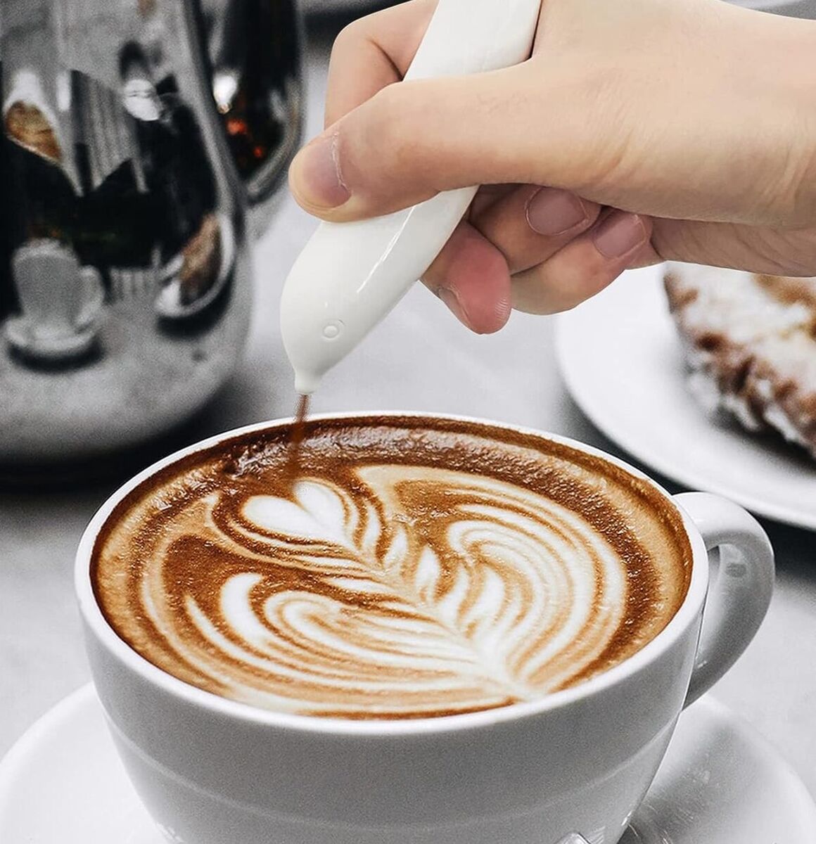 Een close-up van de MagicLatte™ Latte Art Pen, waarmee een kunstzinnig patroon op een kopje koffie wordt getekend.