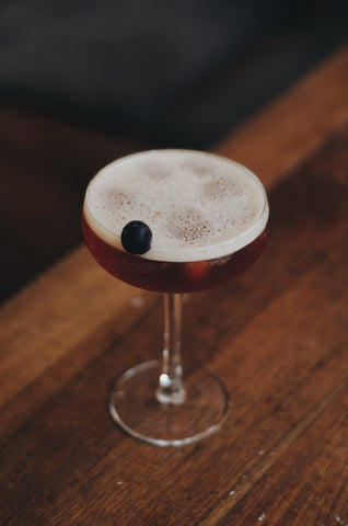 Blueberry flavored CBD drink with sole frozen blueberry garnish in martini glass on wooden bar