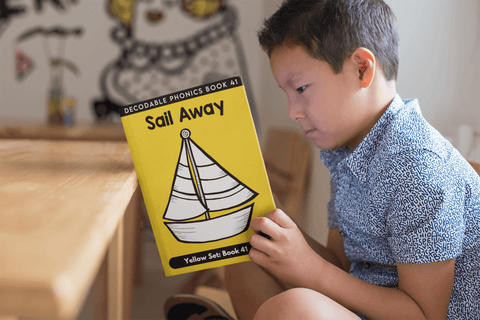 Boy reading a decodable book called Sail Away