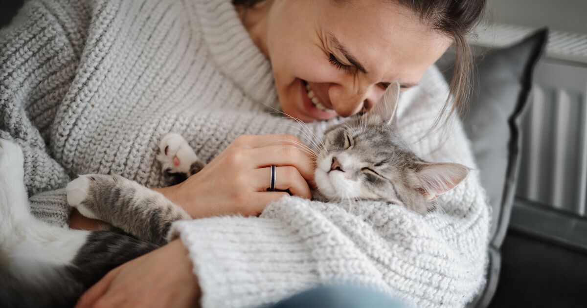 Woman cuddling her grey cat in her arms, smiling.