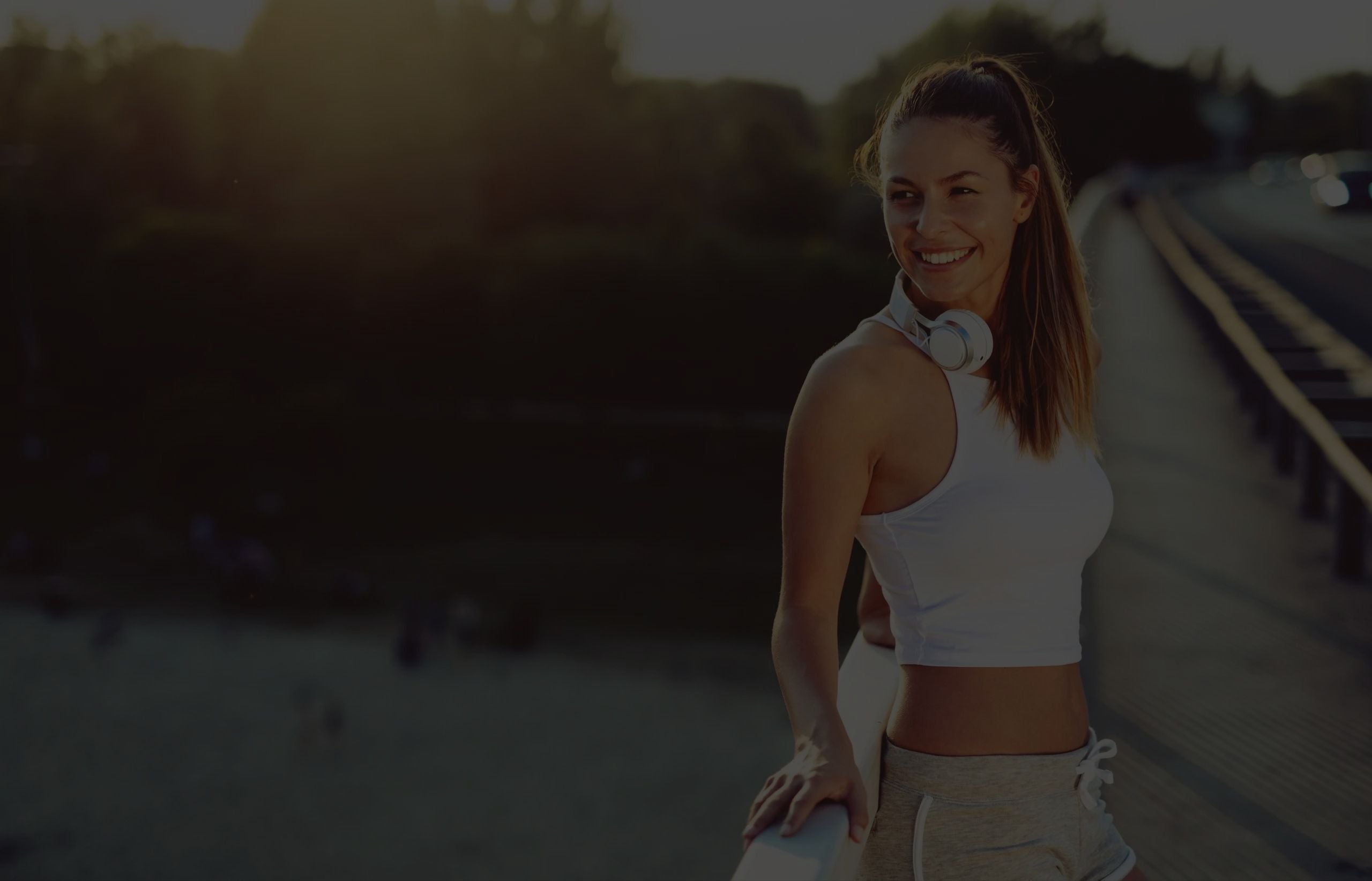 A woman outside on a bridge in the sunset. She´s smiling.