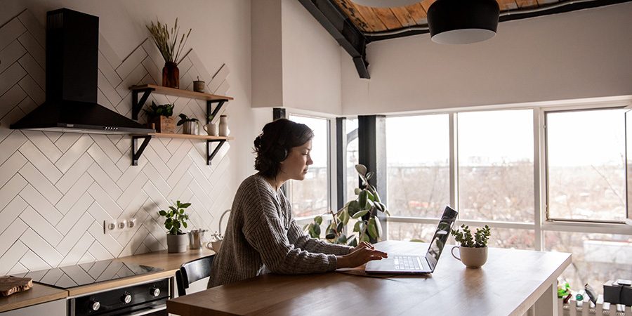 Woman wearing headphones working from a laptop in kitchen